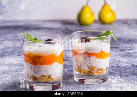 Leichte, gesunde Desserts mit Joghurt, Granola, Chia Seeds in Joghurt, Beeren und Minze in Brille. Verschwommener Hintergrund. Gesundes Frühstückskonzept. Stockfoto