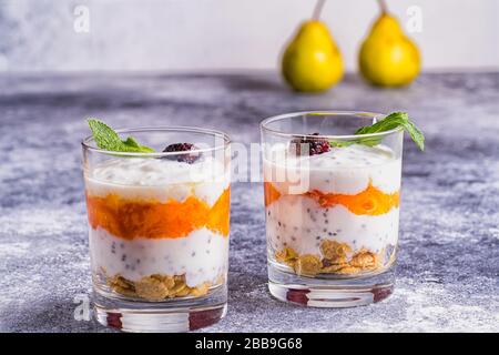 Leichte, gesunde Desserts mit Joghurt, Granola, Chia Seeds in Joghurt, Beeren und Minze in Brille. Verschwommener Hintergrund. Gesundes Frühstückskonzept. Stockfoto