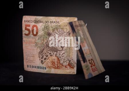 Nahaufnahme von zwei Hälften einer brasilianischen echten Banknote, die aufrecht steht. Studiolebensleben mit niedriger Tonart und schwarzer Oberfläche und dunkelgrauem Hintergrund Stockfoto