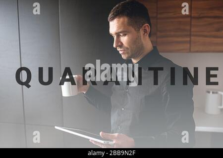 Seitenansicht des jungen Geschäftsmannes in der Küche arbeiten abgelegen. Unternehmer halten Tablette und sehen sich das an. Trinken Sie Tee während der Kaffeepause. Effizientes Arbeiten zu Hause. Stockfoto