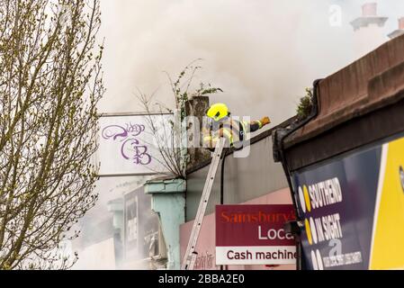 Feuerwehr, die sich während der COVID-19-Sperre mit einem Brand neben Sainsbury's Supermarkt in Westcliff on Sea, Essex, Großbritannien auseinandersetzt. Feuerwehrmann richtet Radio Stockfoto