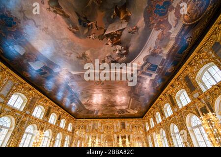 Ein prunkvoller goldener Festsaal im Inneren mit einer farbenfrohen bemalten Decke im Inneren des Rokoko-Katharinenpalastes in Puschkin bei Sankt Petersburg, Russland. Stockfoto