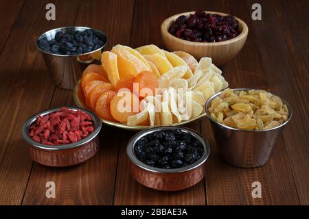 Scheiben von kandierten Ingwerwurzeln, Stücke getrockneter Mango-Früchte, getrocknete Blaubeeren und Goji-Beeren, getrocknete Preiselbeeren, goldene und blaue Rosinen in kleinem b Stockfoto