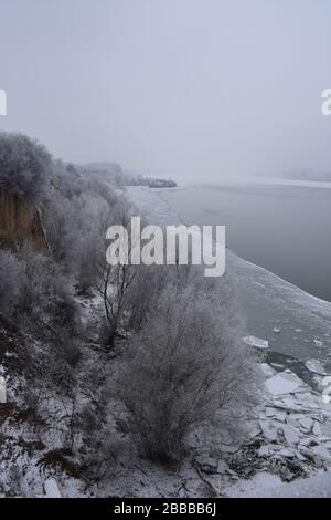 Eine idyllische Winterlandschaft an der Donau. Breiter Fluss und Eis und Eisberge entlang des Ufers, überwachsen mit Bäumen und Sträuchern Stockfoto