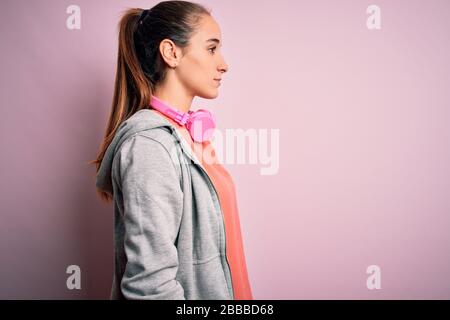 Schöne sportliche Frau, die Sport macht Musik hören, mit Kopfhörern über rosafarbenem Hintergrund, der zur Seite blickt, entspannen Sie sich mit einem natürlichen Gesicht Stockfoto