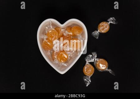 Butterscotch-Süßigkeiten in einer herzförmigen Schüssel auf schwarzem Hintergrund. Stockfoto