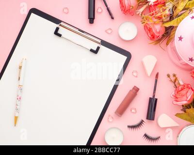 Clipboard- und Makeup-Werkzeuge sowie Kosmetikprodukte und Rosen blühen um sie herum isoliert auf einem pinkfarbenen Hintergrund. Flaches Layout, Kopierbereich in der Draufsicht. Femin Stockfoto