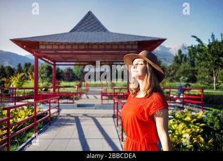 Portrait der schönen Frau in orange Kleid und Hut in der Nähe der Pagode im japanischen Garten Stockfoto