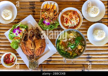 Traditionelle thailändische Küche, gegrillter Fisch, Suppe, Gemüse und Reis auf Bambustisch, Draufsicht. Stockfoto