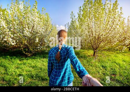 Frau mit roten Haaren Holding ihr Freund von Hand, und was ihn zu dem Garten mit Kirschblüten Bäume bei Sonnenaufgang Stockfoto