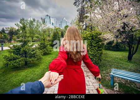 Frau im roten Mantel und Schirm halten sie ihre Freundin und führt zu der Stadtpark mit Cherry Blossom und bedecktem Himmel Stockfoto