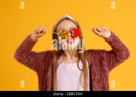 Kleine Mädchen genießen während der Schulpause Lollipops. Glückliche kleine Schüler essen Lollipops. Große wirbelnde Lollipops auf Stöcken Stockfoto