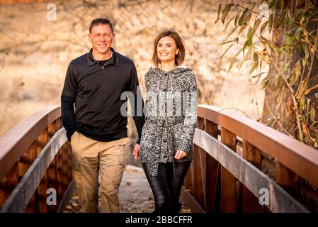 Glückliches Paar lächelt, hält die Hände und geht während der goldenen Stunde auf die Brücke. Stockfoto