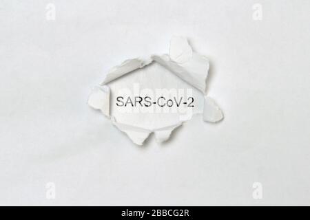 Das Wort sars-cov-2, das in schwarzen Buchstaben auf einem weißen Blatt Papier gedruckt wird, ist in einem Loch sichtbar, das in einem anderen Blatt Papier gerissen ist. Stockfoto