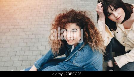 Lässig gekleidete Frauen, die zusammen spazieren und in einer Straße posieren, die bis zur Kamera blickt Stockfoto