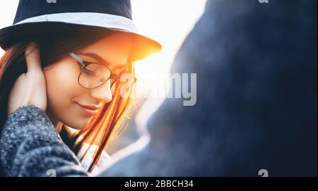 Schöne Frauen mit Hut und Brille, die hinunterschauen, werden von ihrem Liebhaber berührt, der an einem sonnigen Abend posiert Stockfoto