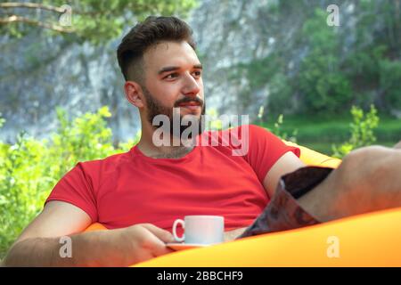 Nahaufnahme des Porträts junger, hübschiger bärtiger Mann, der sich im Freien entspannen und Morgenkaffee trinken kann. Tourismus, Erholung im Freien, aktiver Lebensstil, Geschmack o Stockfoto