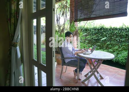 Heimarbeit. Asiatisch-chinesischer Geschäftsmann sitzt und arbeitet am Computer. Gartenhintergrund. Stockfoto