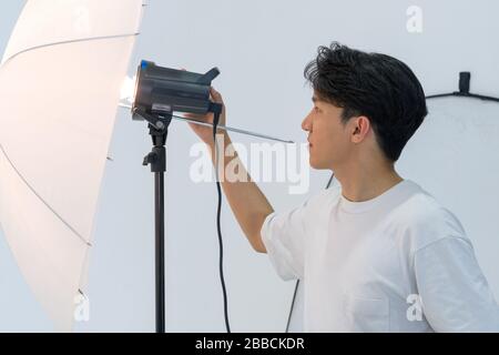 Asiatische Fotografen passen die Helligkeit von Lichtern für die Aufnahme von Modemodellen im Studio an. Stockfoto