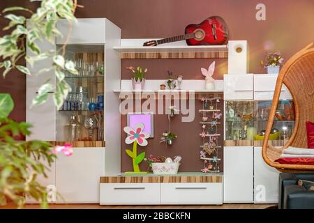 Ein modernes Wohnzimmer ist im Frühling eingerichtet. Das Innenfoto zeigt Blumen, Osterhasen und Ostereier in einer weißen Wandeinheit. Linsenflecken. Stockfoto