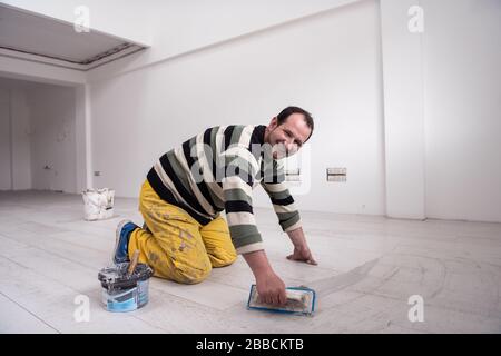 Verfugen von Keramikfliesen. Tiler füllen den Raum zwischen Keramikfliesen aus Holz mit einem Gummi-Trowel auf dem Boden in einer neuen modernen Wohnung Stockfoto