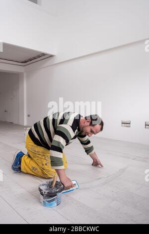 Verfugen von Keramikfliesen. Tiler füllen den Raum zwischen Keramikfliesen aus Holz mit einem Gummi-Trowel auf dem Boden in einer neuen modernen Wohnung Stockfoto