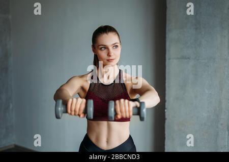 Attraktive Passform junge Frau im Sport tragen lächelnde Mädchenzüge mit Hanteln im Loft-Studio Stockfoto