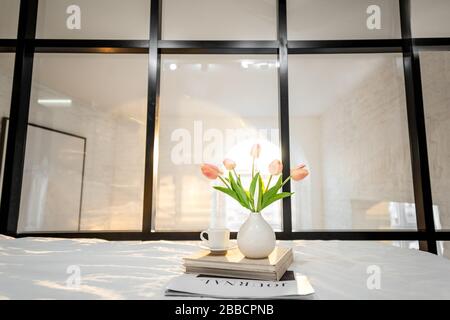 Sonniges Schlafzimmer mit Blumen, Büchern und Kaffeetasse. Romantische Schlafzimmer-Atmosphäre und gutes Morgenkonzept Stockfoto