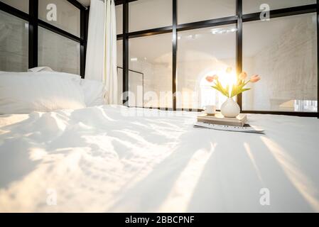 Sonniges Schlafzimmer mit Blumen, Büchern und Kaffeetasse. Romantische Schlafzimmer-Atmosphäre und gutes Morgenkonzept Stockfoto