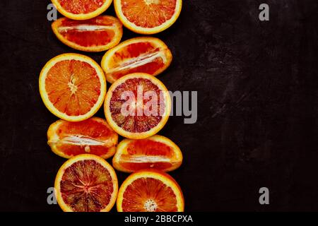 Draufsicht über frische orangefarbene Bluthälften und Quater auf schwarzem Hintergrund mit Kopierbereich. Getontes Bild Stockfoto