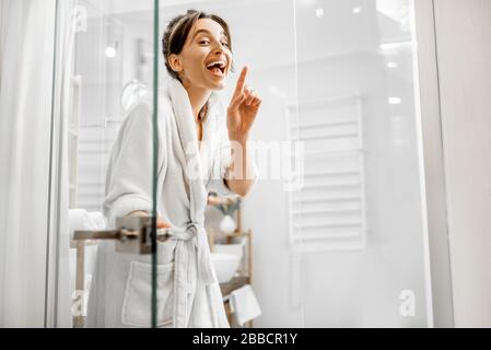 Junge und freudige Frau im bademantel, die ins Bad geht und zu Hause eine Glastür schließt Stockfoto