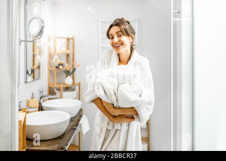 Junge Frau im bademantel, die etwas Hausarbeit macht und im Badezimmer mit Handtüchern steht Stockfoto