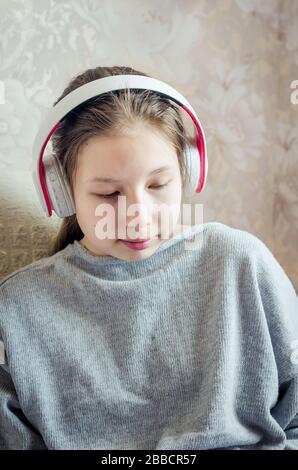 Teenager-Mädchen in Kopfhörern auf dem Sofa sitzen, hört eine Lektion, Podcast, Musik, kommuniziert in sozialen Netzwerken Konzept Online-Lernen, Bildung a Stockfoto