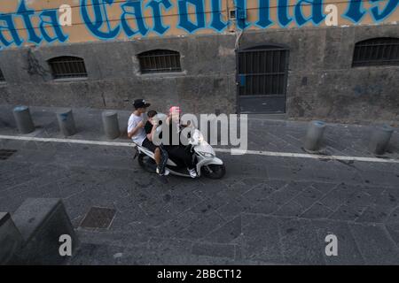 Drei Personen fahren illegal auf einem Roller ohne Helm durch die Straßen von Neapel Stockfoto