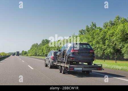 Schwarz zerbrochenes Auto nach Unfall auf Schleppfahrzeug. Auto auf Auto Carrier Trailer auf Autobahn transportiert. Stockfoto