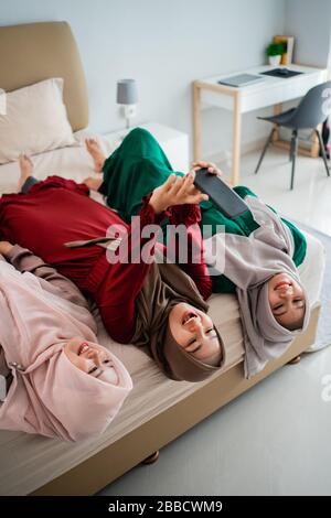 Drei verschleierte Frauen legten sich auf und die Hände hoben sich auf das Bett, während sie zusammen mit dem Kamerasmartphone eine selfie nahmen Stockfoto