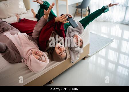 Drei verschleierte Frauen legten sich auf und die Hände hoben sich auf das Bett, während sie zusammen mit dem Kamerasmartphone eine selfie nahmen Stockfoto