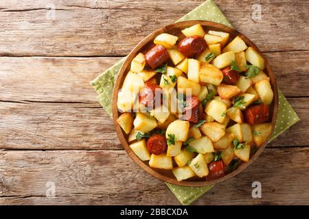 Hausgemachte Speisen Bratkartoffeln mit Würstchen und Kräutern liegen in einem Teller auf dem Tisch. Horizontale Draufsicht von oben Stockfoto