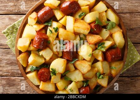 Leckere knusprige Bratkartoffeln mit Würstchen und Kräutern liegen in einem Teller auf dem Tisch. Horizontale Draufsicht von oben Stockfoto