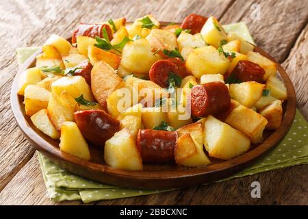 Duftende Bratkartoffeln mit gegrillten Würstchen und Kräutern liegen in einem Teller auf dem Tisch. Horizontal Stockfoto