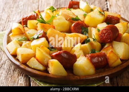 Hausgemachte Speisen Bratkartoffeln mit Würstchen und Kräutern liegen in einem Teller auf dem Tisch. Horizontal Stockfoto