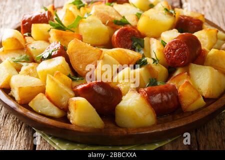 Leckere knusprige Bratkartoffeln mit Würstchen und Kräutern liegen in einem Teller auf dem Tisch. Horizontal Stockfoto