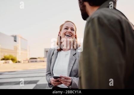 Porträt einer erfolgreichen und lachenden Geschäftsfrau im Gespräch mit männlichen Lebensgefährten auf der Straße der Stadt Stockfoto