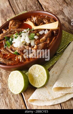 Mexikanische Birria de res serviert mit Kalk und Tortilla Close-Up in einer Schüssel auf dem Tisch. Vertikal Stockfoto