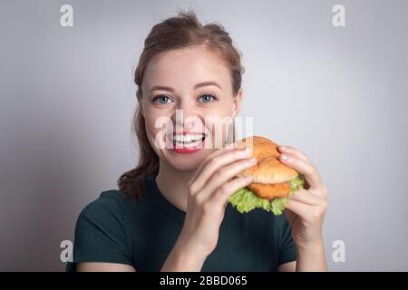 Lächelndes Mädchen der jungen kaukasischen Frau, das Hühnerburger isst Stockfoto