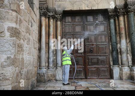 Jerusalem. März 2020. Ein Arbeiter reinigt die verschlossene Tür der Grabeskirche in der Altstadt von Jerusalem inmitten einer Coronavirus-Epidemie am 30. März 2020. Credit: Muammar Awad/Xinhua/Alamy Live News Stockfoto