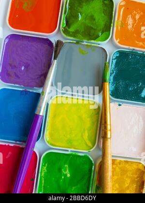 Draufsicht auf zwei Lackpinsel, die auf einer Wasserfarbenpalette für Kinder liegen Stockfoto