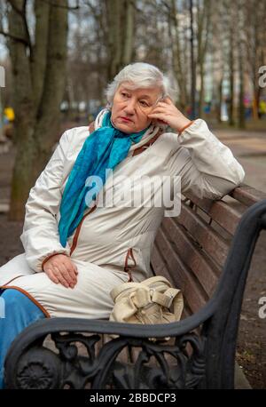 Eine elegante ältere grauhaarige Frau sitzt auf einer Parkbank. Stockfoto