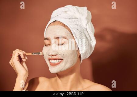 Close-up Portrait von schöne asiatische Mädchen in Spa mit einem Handtuch auf dem Kopf, Gesichts Clay Mask. Stockfoto