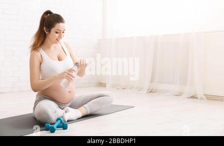 Junge schwangere Frau trinkt während des Yoga-Trainings Wasser Stockfoto